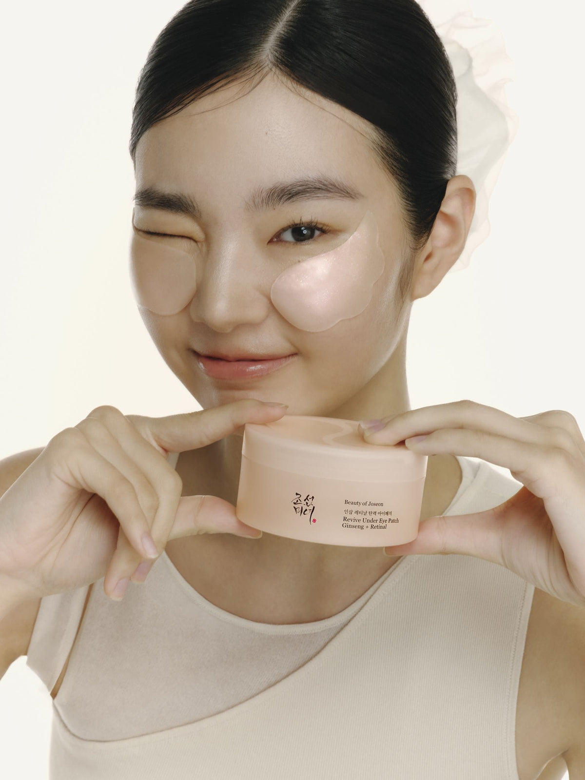 Model met Beauty of Joseon Revive Under Eye Patch onder haar oog en de pot in haar handen