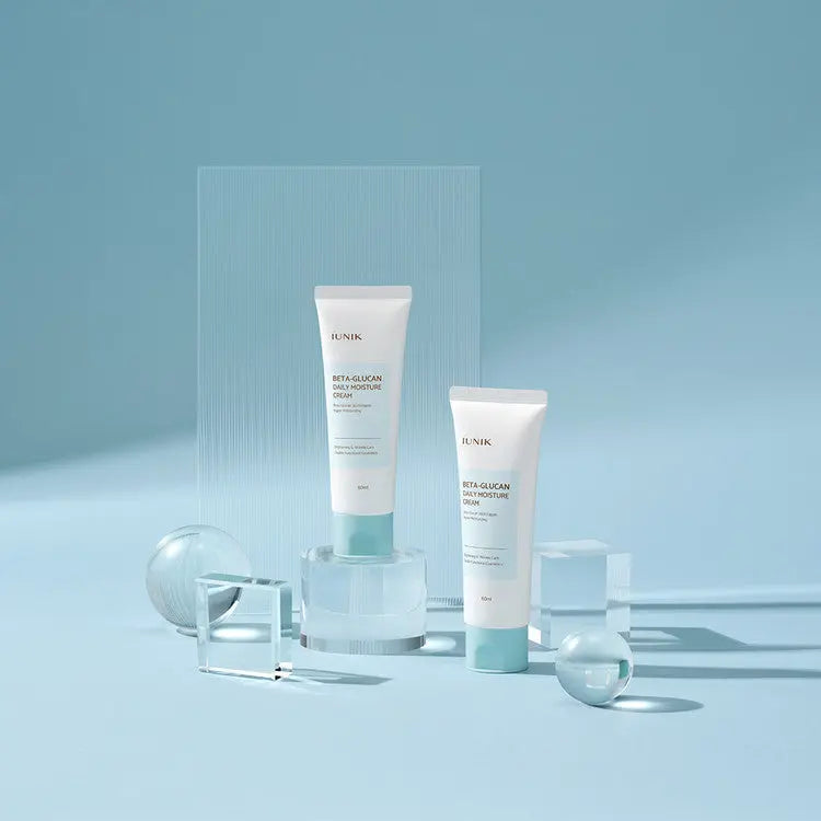 iUNIK Beta-Glucan Daily Moisture Cream, twee tubes op glazen blokjes tegen blauw