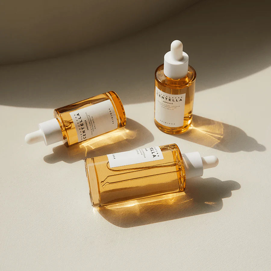 Drie flesjes SKIN1004 Madagascar Centella Ampoule liggend en staand gerangschikt op een beige ondergrond met zachte schaduwen