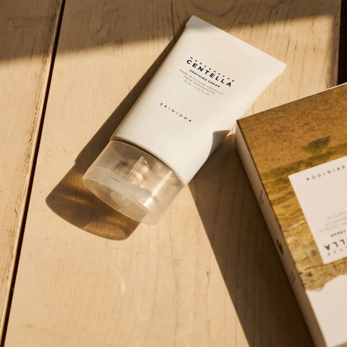 SKIN1004 Centella Soothing Cream met verpakking op een houten ondergrond in zonlicht